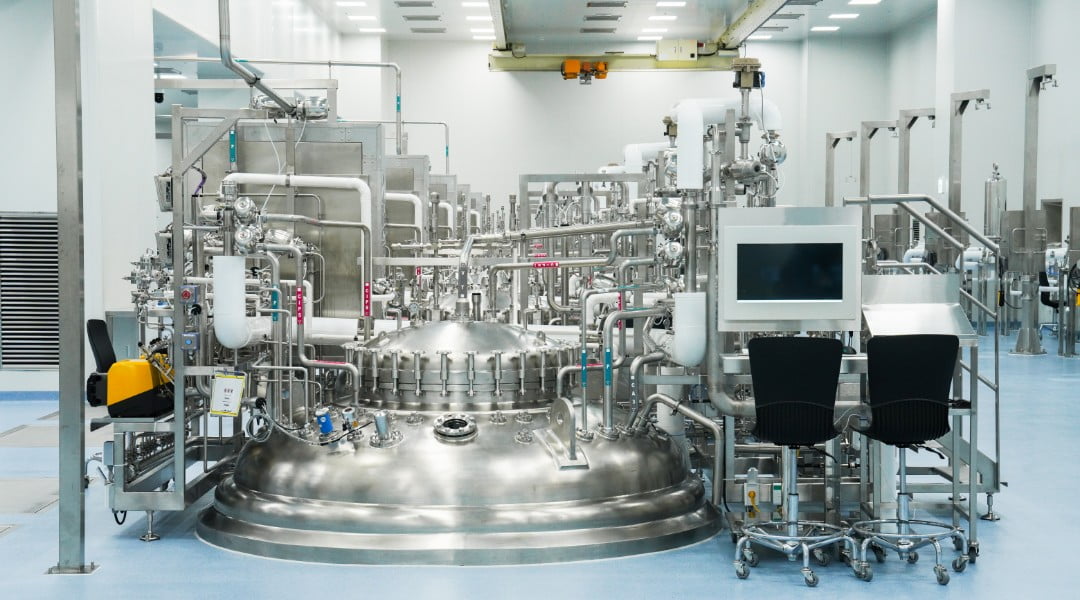 Front view of a biotech manufacturing facility with complex piping and a large reactor.