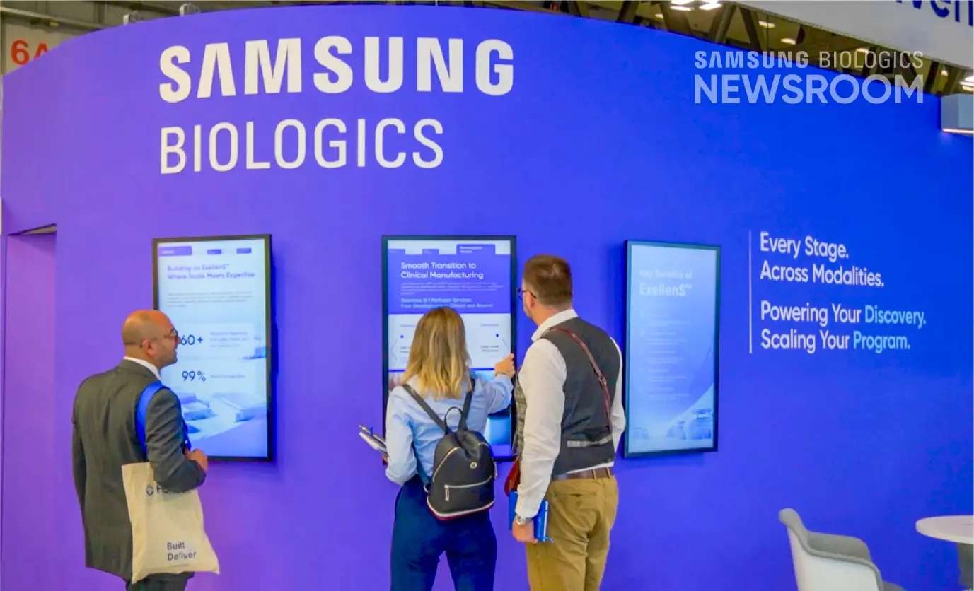 Visitors interacting with digital display screens at the Samsung Biologics booth at CPHI, featuring ExellenS content